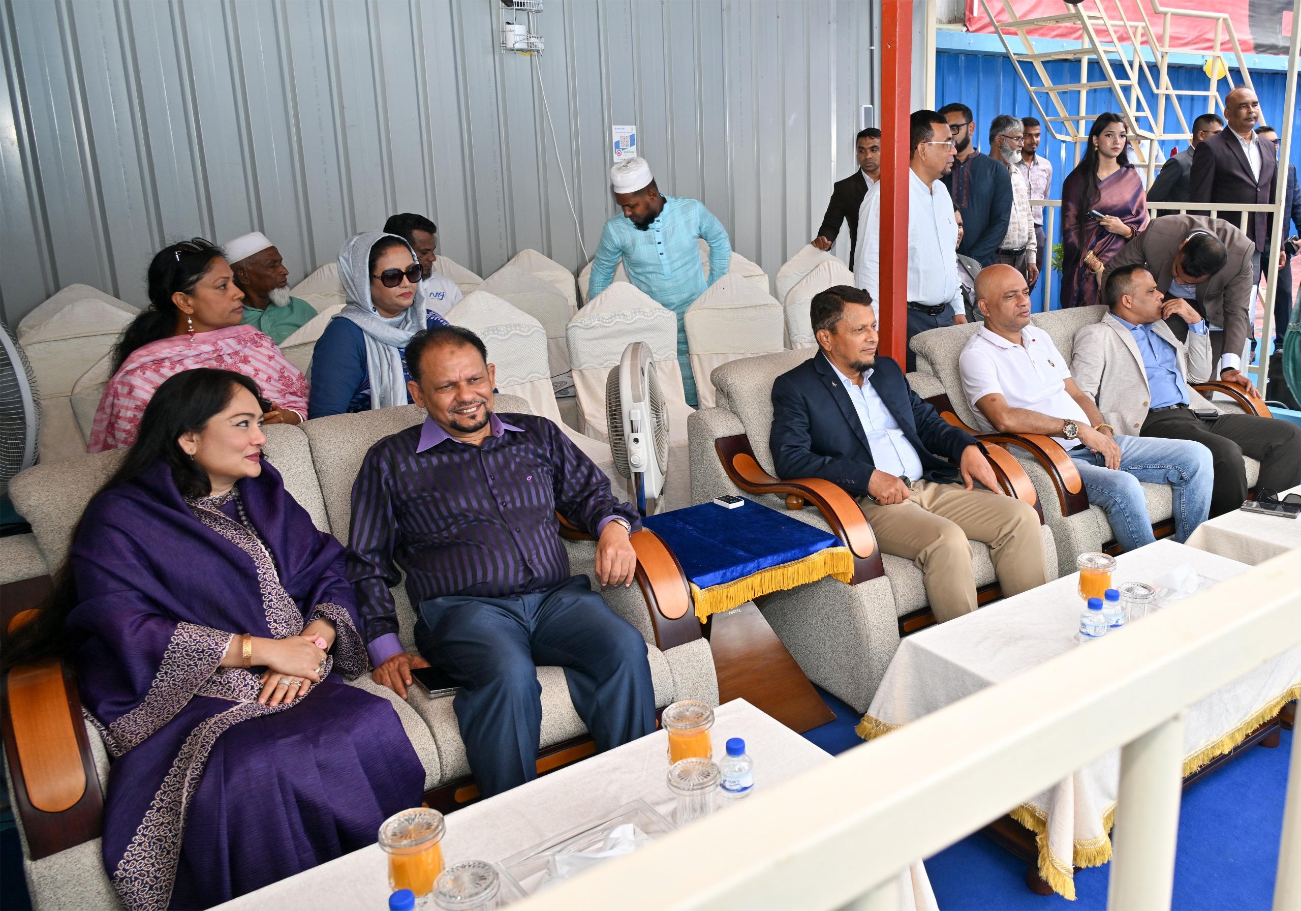 Rows of invited guests in upholstered chairs watch the opening ceremony from a covered gallery beside the pool.