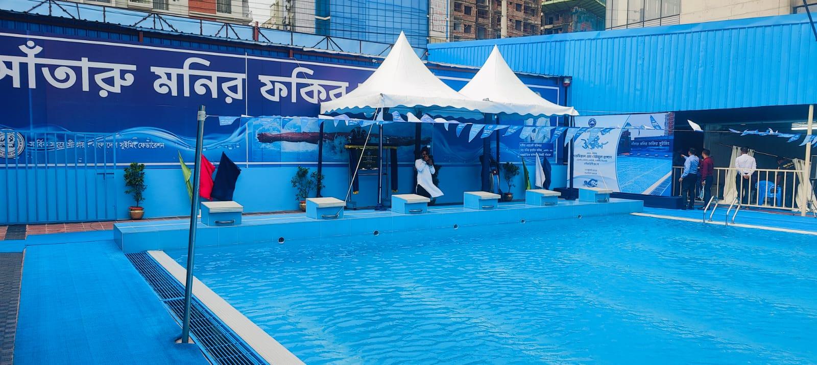 The starting blocks and diving platform at the pool's head, dressed with event banners, red and navy flags, and a Bangladesh Swimming Federation backdrop.