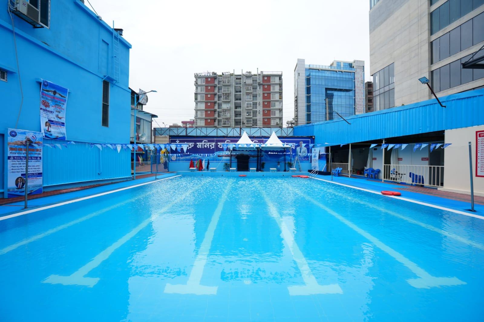 Lane markers painted on the pool floor lead toward the shaded starting-block platform under twin white canopies.