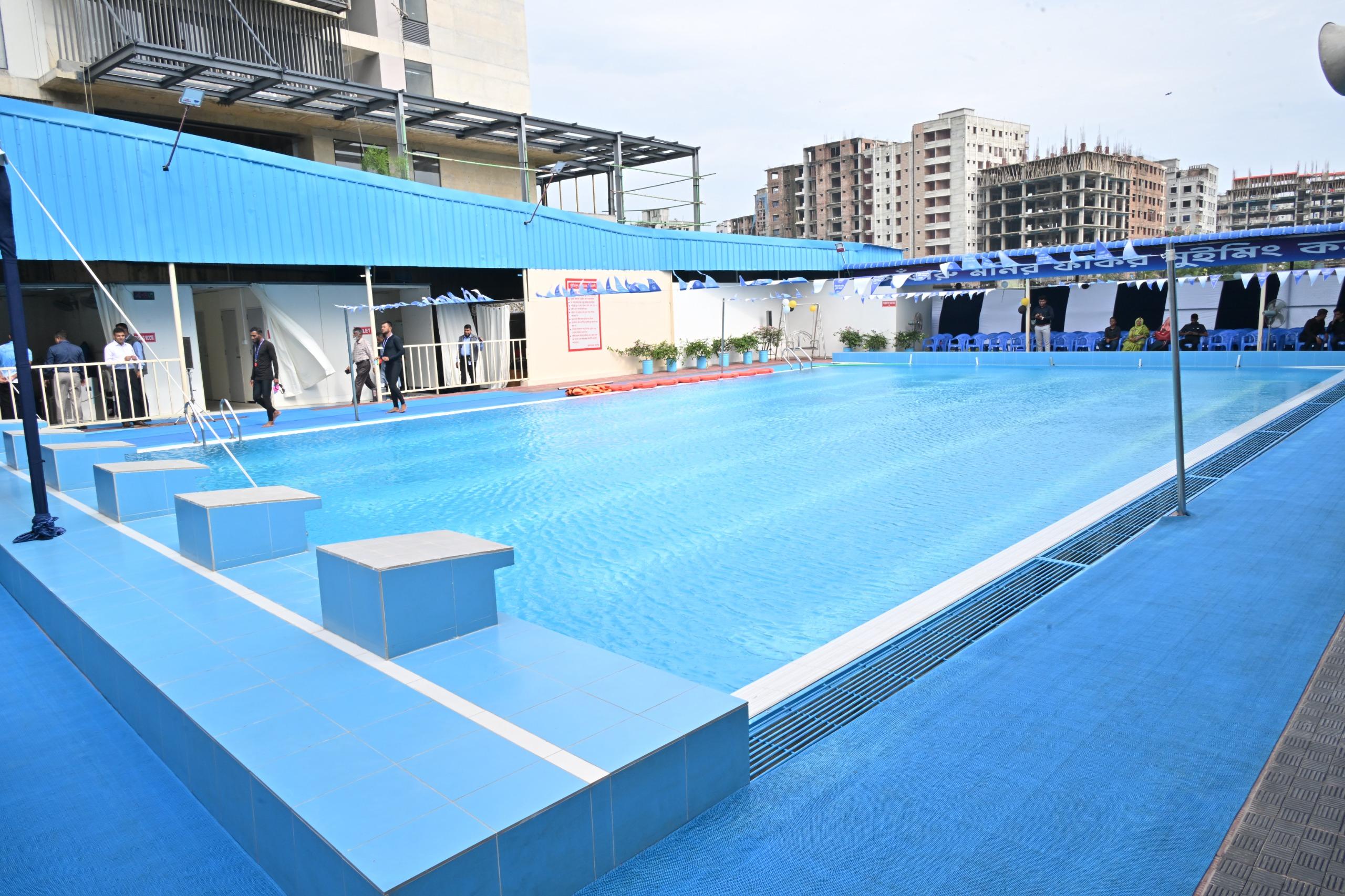 The outdoor pool at Monir Fokir Swimming Complex, lane ropes stretched across turquoise water beneath the rooftop deck.